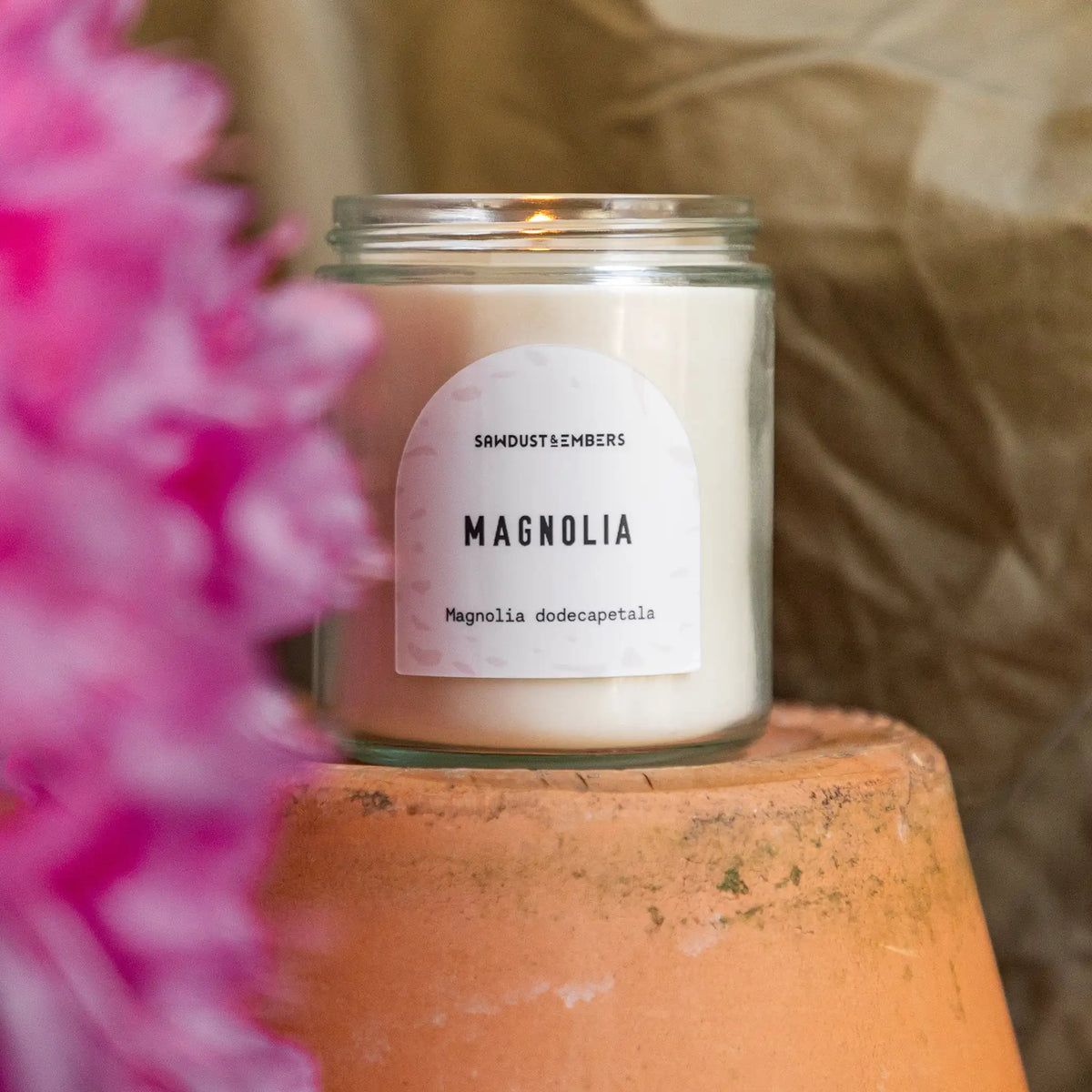 Magnolia candle styled with flowering blooms and warm natural textures.