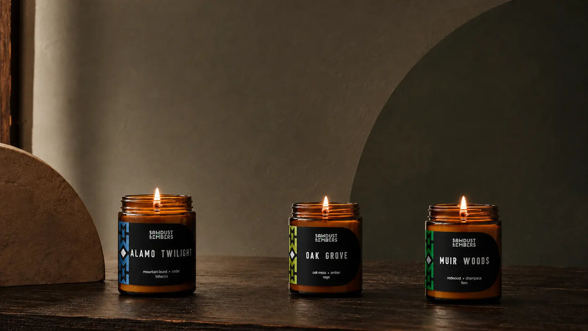 Lit Alamo Twilight and Oak Grove amber candles arranged with wood, stone, and natural textures